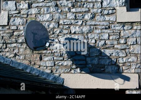 Satellitenschüssel auf Steinwand des Hauses. Queen's Road, Fellside, Kendal, Cumbria, England, Vereinigtes Königreich, Europa. Stockfoto