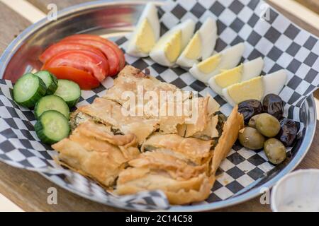 Draufsicht auf einen Teller, mit hausgemachtem traditionellen türkischen Stil Tabla Borek, gekochte Eier, Joghurt, geschnittenes Gemüse und Oliven, über einem schwarzen und weißen pa Stockfoto