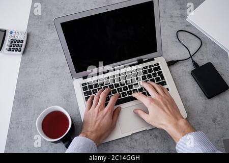 Geschäftsmann nutzt Laptop und analysiert die Finanzinformationen in seinem Büro. Nahaufnahme der männlichen Hände, die auf der Computertastatur tippen. Stockfoto