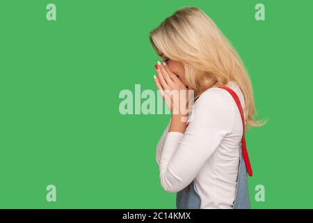 Seitenansicht der unglücklichen erwachsenen Frau in Denim Overalls weinen vor Traurigkeit, leiden Depression und Einsamkeit, negative Emotion, frustriert durch misfortun Stockfoto