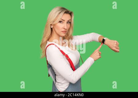 Es ist spät, Zeit zu gehen! Porträt von herrisch strengen erwachsenen Frau in stilvollen Overalls zeigt auf Armbanduhr und Blick mit unzufrieden ungeduldig expressi Stockfoto