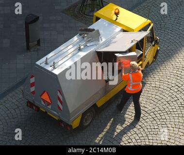 Kleiner Müllwagen mit Arbeiterin in der Einkaufsstraße. Sie wirft im Auftrag einer niederländischen Gemeinde Abfälle vom Markt in einem LKW Stockfoto