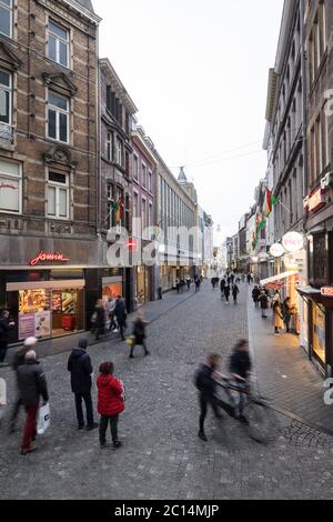 Blick auf die Grote Straat in Maastricht, Niederlande, mit beleuchteten Geschäften und Einkaufsbummel am Ende des Nachmittags Stockfoto