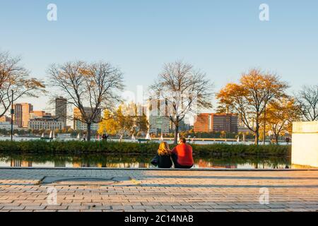 Boston, USA - Oktober 13 2014; Paar sitzt auf der Esplanade neben der Storrow Lagune in der späten Nachmittagssonne an einem Herbsttag mit Charles River und Stadt im Leben Stockfoto