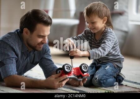 Glücklicher Vater und kleiner Sohn spielen mit Spielzeugauto zusammen Stockfoto