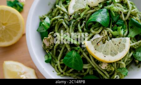 Vegane Pasta mit Avocado-Dip-Sauce, Spinatblättern und Zitrone in weißer Schüssel. Auf Holzhintergrund. Vegetarisch gesunde Lebensmittel Stockfoto