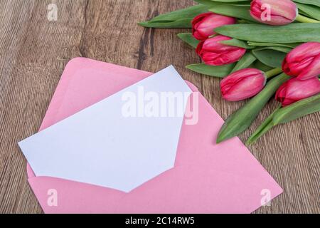 Umschlag mit Blatt Papier und Tulpen auf einem Holzhintergrund Stockfoto