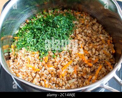 Fein gehackte Grüns zu Buchweizen mit Gemüse hinzufügen. Brei mit Gemüse kochen. Stockfoto