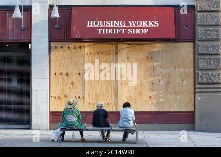 Menschen sitzen auf einer Bank vor einem verschlossenen, vertauften, geschlossenen, Housing Works Thrift Shop in Manhattan, New York, NY. 6. Juni 2020. Stockfoto