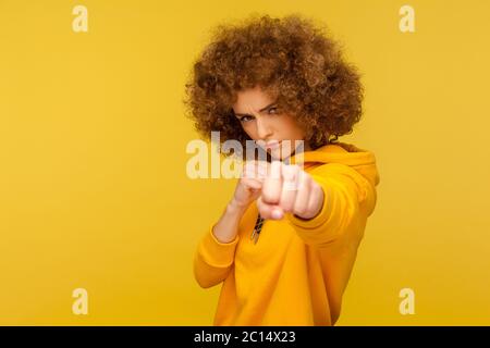 Kampf und Kampfgeist. Portrait einer aggressiven lockigen Frau im urbanen Stil Kapuzenpullover, die mit geballten Fäusten angreift und zu schlagen droht. ind Stockfoto