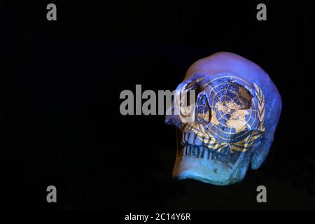 Das UN-Symbol-Logo der Vereinten Nationen projiziert über einen Totenkopf isoliert auf einem schlichten schwarzen Hintergrund. Stockfoto