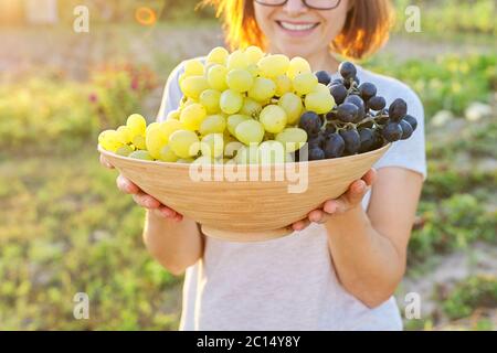 Frau mit Schale frisch gepflückten blauen und grünen Trauben, sonnigen Garten Hintergrund Stockfoto