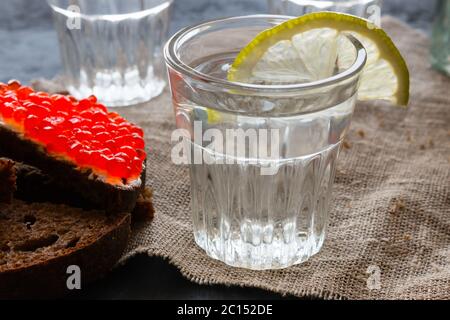 Glas Wodka mit Zitronenscheibe aus der Nähe und Sandwich mit rotem Kaviar Stockfoto
