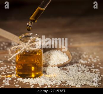 Frisches Sesamöl in einer Glasflasche und Samen in einem Holzlöffel Stockfoto