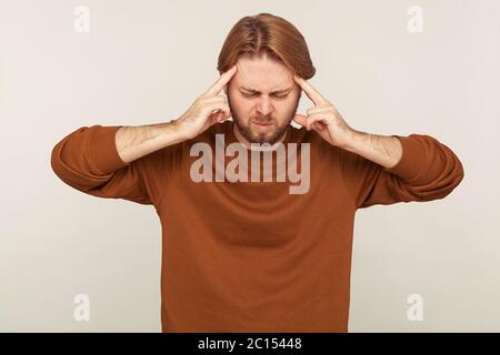 Porträt von ungesunden bärtigen Mann in Sweatshirt klammernden Wunden Kopf Schläfen, Gefühl unwohl und Leiden unerträgliche Kopfschmerzen, Migräne von Stress, Dutzende Stockfoto