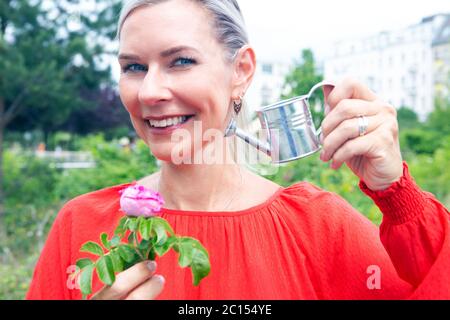 Portrait der blonden Frau Bewässerung mit Miniatur kann eine Blume Stockfoto