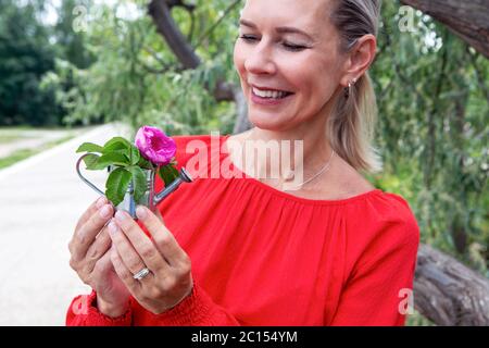 Portrait der blonden Frau im Freien hält eine Miniatur Gießkanne mit einer Blume Stockfoto