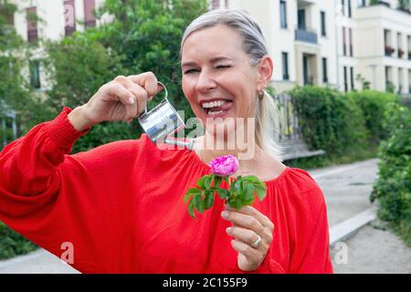 Portrait der blonden Frau Bewässerung mit Miniatur kann eine Blume und macht lustige Gesicht Stockfoto