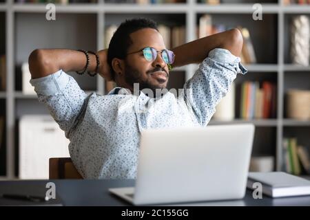 Afrikanischer Geschäftsmann streckt sich in einem Bürostuhl und blickt aus dem Fenster Stockfoto