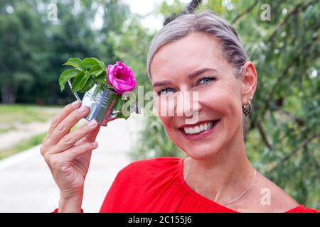Portrait der blonden Frau im Freien hält eine Miniatur Gießkanne mit einer Blume Stockfoto