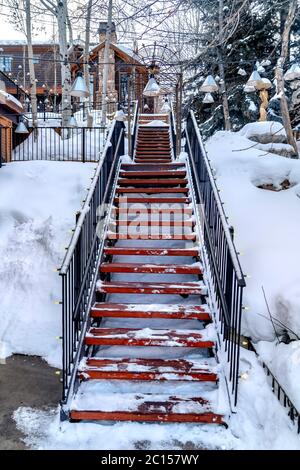 Treppe auf verschneiten Hang mit Gebäuden und Bäumen unter bewölktem Winterhimmel Stockfoto