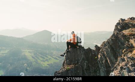 Junger Mann mit Rucksack auf Felsen sitzend und in die Landschaft schauend. Dem Schweigen zuhören. Schöner Moment das Wunder der Natur. Stockfoto