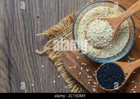 Weiße Sesamsamen in einem Holzlöffel und schwarzer Sesam auf Holzblock. Weißer Sesam hilft Knochen und Zähne zu stärken. Schwarzer Sesam hilft zu verbrennen und Stockfoto