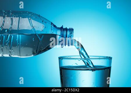 Wasser aus einer Flasche wird auf blauem Hintergrund in ein Glas gegossen. Gesundes Lifestyle-Konzept. Stockfoto