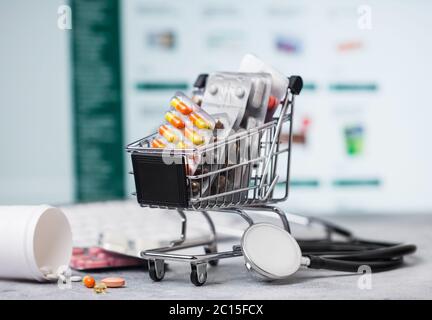 Einkaufswagen mit Medikamenten zum Online-Kauf mit Tastatur und Stethoskop auf hellem Hintergrund. Vitamine und Antibiotika Pillen mit Schmerzmitteln Stockfoto