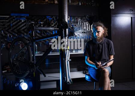 Stilvolle Fahrrad Mechaniker Notizen in Zwischenablage in der Werkstatt. Thema Kleinunternehmen Verkauf, Reparatur und Service Fahrräder. Techniker Stockfoto