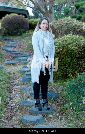 Ziemlich gemischte Rennen 40-49 Jahre alte Frau trägt Brille lächelnd. Ganzkörperansicht von vorne. Vertikale Aufnahme. Stockfoto