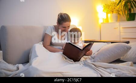 Junge lächelnde Mutter mit kleinen Kleinkind Sohn Buch im Bett zu lesen Stockfoto