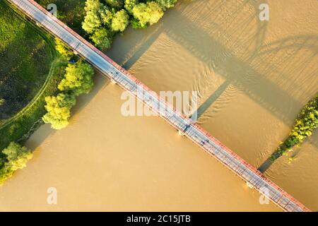 Luftaufnahme einer schmalen Straßenbrücke, die sich über einen schlammigen, breiten Fluss in grüner ländlicher Umgebung erstreckt. Stockfoto