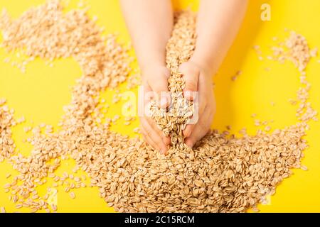 Gesunde Ernährung. Rohe Haferflocken in Kinderhände, die in den sicheren Händen des Elternteils von oben eingeschlossen sind. Horizontale Ausrichtung Stockfoto