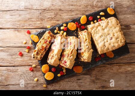 In Scheiben geschnittener zuckerloser Obstkuchen mit getrockneten Aprikosen Beeren Rosinen Feigen Kirschen in der Nähe auf einem Schieferbrett auf dem Tisch. Horizontale Draufsicht von oben Stockfoto