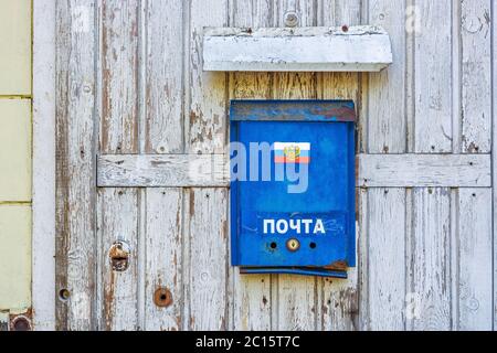 Alte rostblaue Briefkasten mit dem Emblem der russischen Post an der alten Tür eines Wohnhauses mit abblätternder Farbe. Übersetzung: 'Post'. Stockfoto