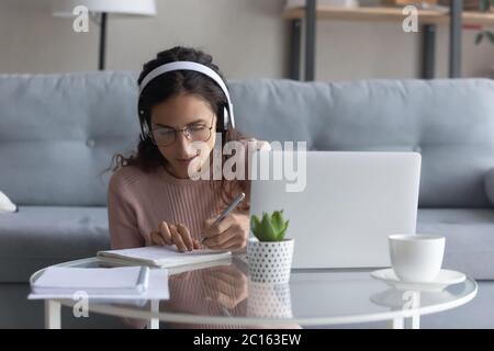Fokussierte Frau mit Kopfhörern, die Schulaufgaben macht, mit Laptop Stockfoto