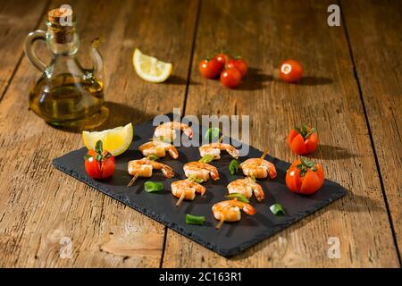 Garnelen Spieße mit Tomaten, Zitrone und Öl auf einem Stein Stockfoto