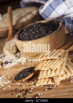 Frisches Sesamöl in einer Glasflasche und Samen in Holzschüssel und Löffel Stockfoto