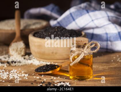 Frisches Sesamöl in einer Glasflasche und weiße und schwarze Samen in Holzschüsseln Stockfoto