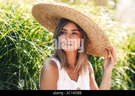 Porträt einer jungen Frau im Strohhut, die in einem Park sitzt Stockfoto