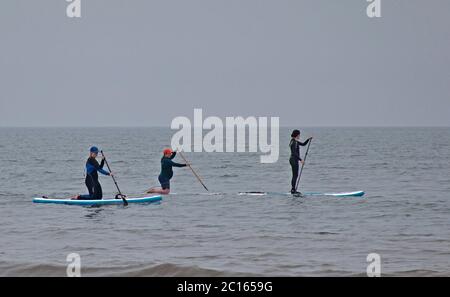 Portobello, Schottland, Großbritannien. 14. Juni 2020. Nach dem gestrigen Nebel den ganzen Tag, wurde es heute etwas heller und wärmer, aber immer noch dreich mit bewölktem Himmel, Temperatur von 16 Grad Celsius. Geschäftiges Meer mit allen Cafés und Pub geöffnet, im Bild: Drei weibliche Paddle-Boarder und eine Familie am Meer. Stockfoto