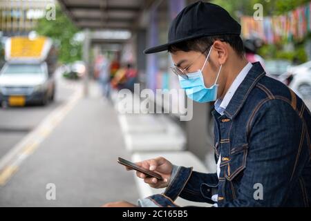 Asian Young man mit Smartphone in der Stadt und trägt Gesichtsmaske zum Schutz der Luftverschmutzung, Partikel und zum Schutz Grippevirus, Influenza Stockfoto