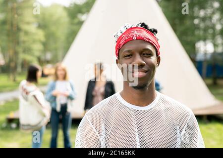 Portrait eines lächelnden, hübschen jungen schwarzen Mannes mit Bart, der rote Bandanas trägt und Zeit auf dem Festivalcampingplatz verbringt Stockfoto