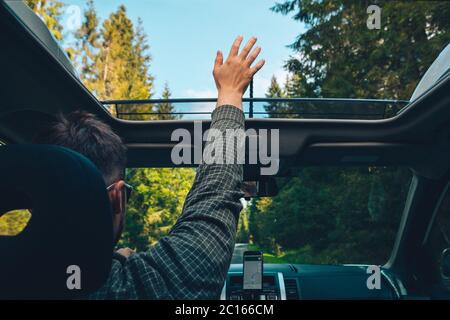 Der Mann fängt beim Autofahren mit der Hand durch das geöffnete Schiebedach Stockfoto
