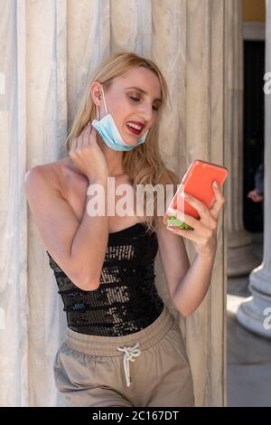 Beautifil blonde Mädchen lächelt mit Gesichtsmaske nach Lockdown Wiedereröffnung - sie genießt ihren Spaziergang Spaß, chating mit Freunden, Selfies outsi Stockfoto