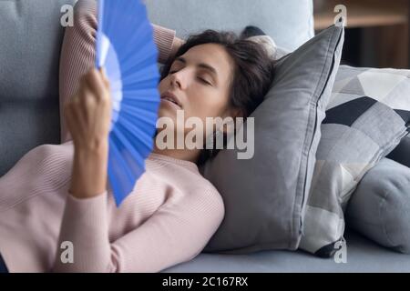 Erschöpft überhitzte Frau winkend Papierventilator, liegend auf Couch Stockfoto