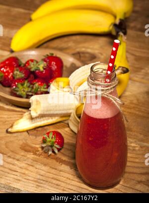 Erdbeer- und Bananenmoothie oder Milchshake in der Flasche auf Holzgrund. Stockfoto