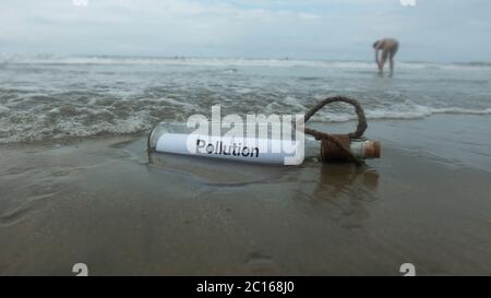 Verschmutzungsmeldung in der Glasflasche, die von der verlassenen Flut am Strand im Sand begraben wurde Stockfoto