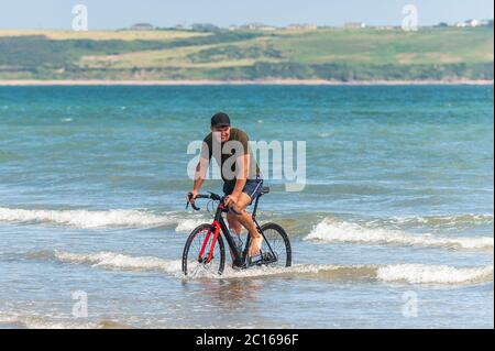 Tramore, Co. Waterford, Irland. Juni 2020. Tramore Beach war heute an einem herrlich sonnigen Tag mit Höhen von 18 bis 23 Grad Celsius voll. Ein Mann fährt mit seinem Fahrrad ins Meer, um sich abzukühlen. Quelle: AG News/Alamy Live News Stockfoto